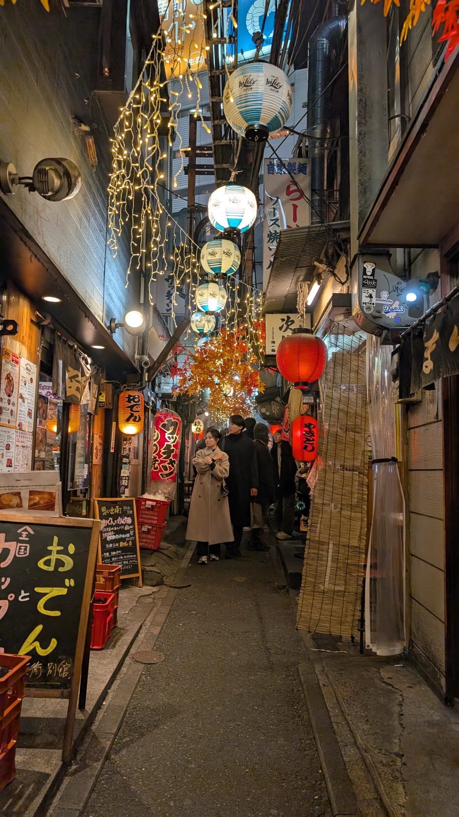 A narrow Tokyo alley strung with paper lanterns and fairy lights, lined with small restaurants